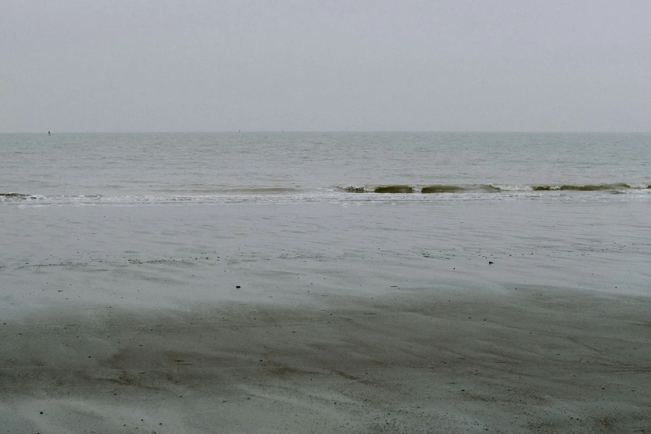 Gentle waves crossing an empty beach beneath grey sky.
