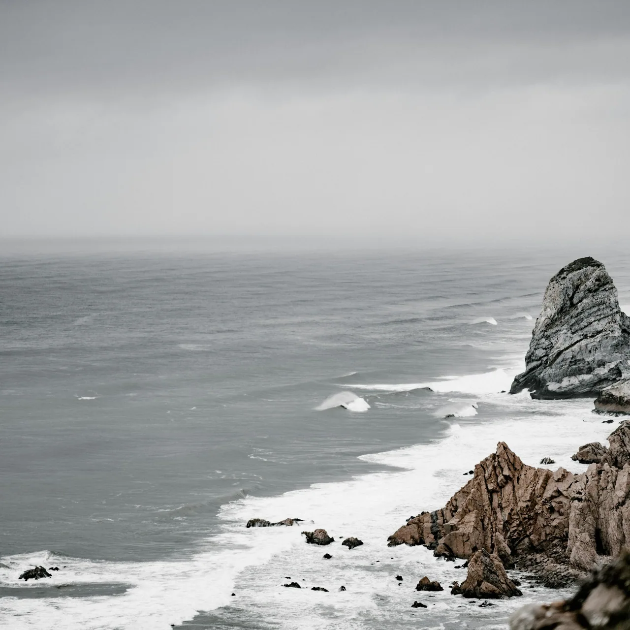 Dark coastal rock meeting a calm grey sea.